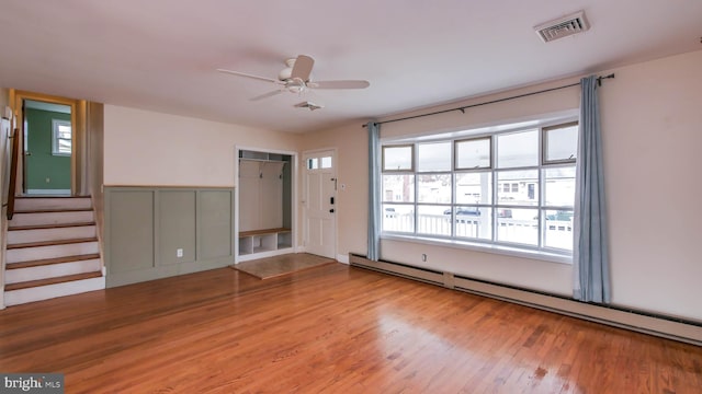 interior space featuring stairway, a ceiling fan, wood finished floors, visible vents, and baseboard heating