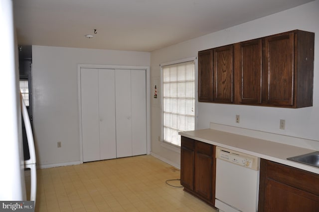 kitchen featuring light floors, light countertops, dark brown cabinetry, dishwasher, and baseboards