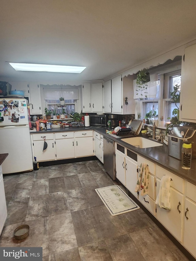 kitchen with dark countertops, stainless steel dishwasher, freestanding refrigerator, white cabinetry, and a sink