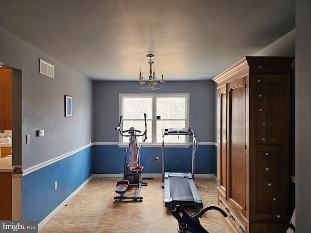 exercise room with baseboards, wood finished floors, visible vents, and an inviting chandelier