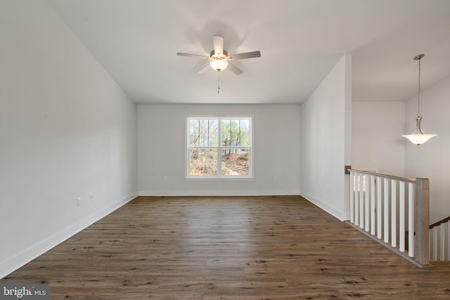 empty room with wood finished floors, a ceiling fan, and baseboards