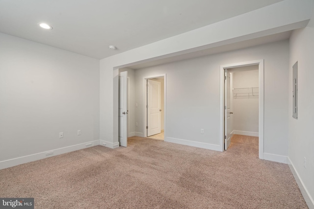 unfurnished bedroom featuring recessed lighting, light colored carpet, baseboards, a spacious closet, and electric panel