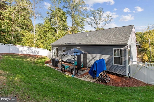 rear view of house featuring a patio area, a fenced backyard, roof with shingles, and a yard