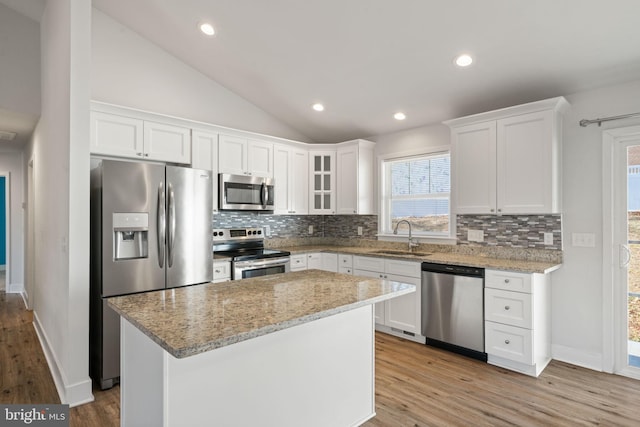 kitchen featuring lofted ceiling, a center island, stainless steel appliances, white cabinetry, and a sink