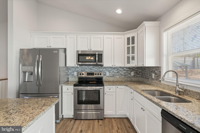 kitchen with appliances with stainless steel finishes, vaulted ceiling, white cabinets, and a sink