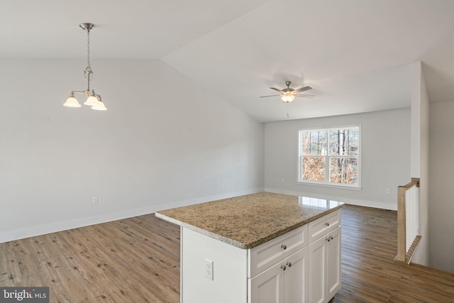 kitchen featuring wood finished floors, white cabinets, open floor plan, light stone countertops, and decorative light fixtures