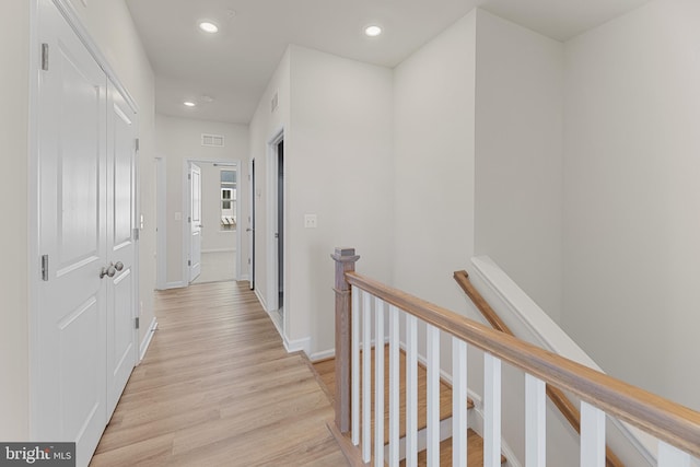 hallway with light wood finished floors, visible vents, baseboards, an upstairs landing, and recessed lighting