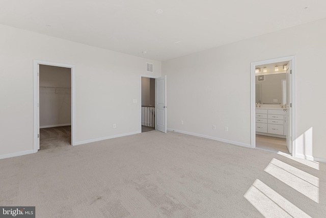 unfurnished bedroom featuring connected bathroom, light colored carpet, visible vents, baseboards, and a spacious closet