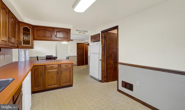 kitchen featuring visible vents, white appliances, a peninsula, brown cabinetry, and glass insert cabinets