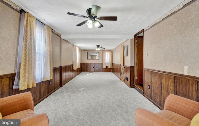 empty room with ceiling fan, wooden walls, carpet, and wainscoting