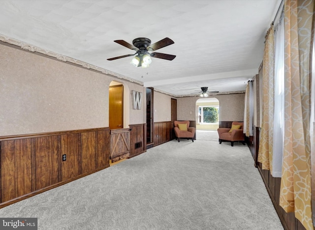 unfurnished room featuring arched walkways, wooden walls, wainscoting, and carpet