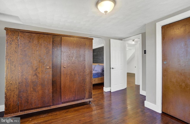 unfurnished bedroom with dark wood finished floors, arched walkways, and baseboards