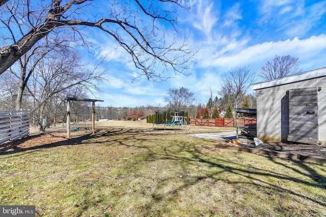 view of yard featuring a fenced backyard, an outbuilding, playground community, and a trampoline