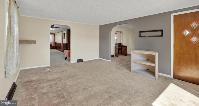 unfurnished living room featuring baseboards, ornamental molding, carpet floors, arched walkways, and a ceiling fan