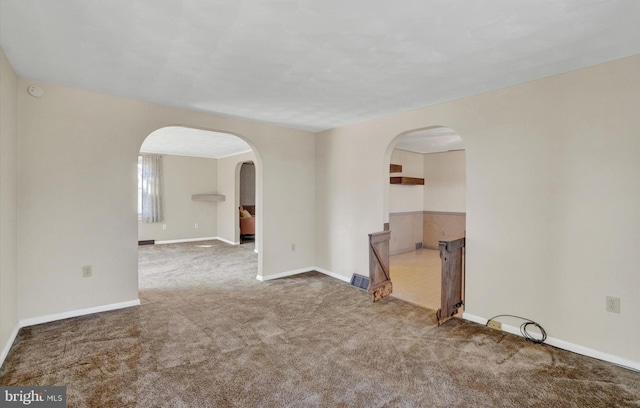 carpeted spare room with baseboards and arched walkways