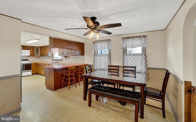 dining space featuring ornamental molding, arched walkways, brick patterned floor, and ceiling fan