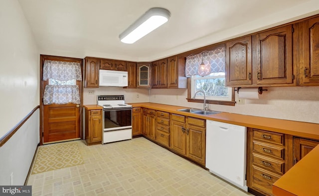 kitchen featuring brown cabinets, white appliances, light countertops, and a sink