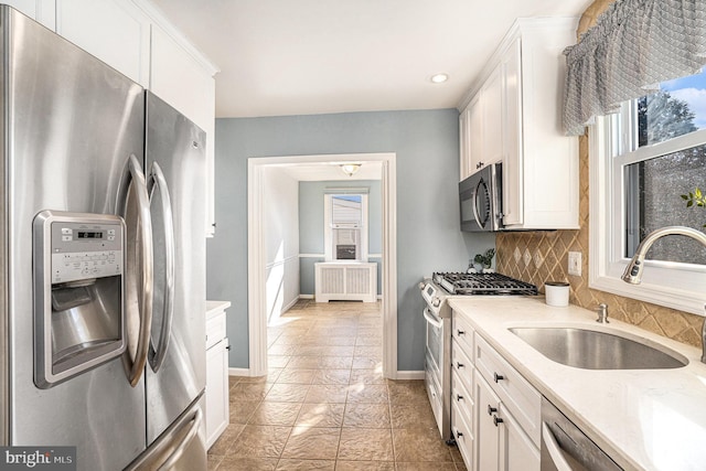 kitchen featuring tasteful backsplash, white cabinets, radiator heating unit, stainless steel appliances, and a sink