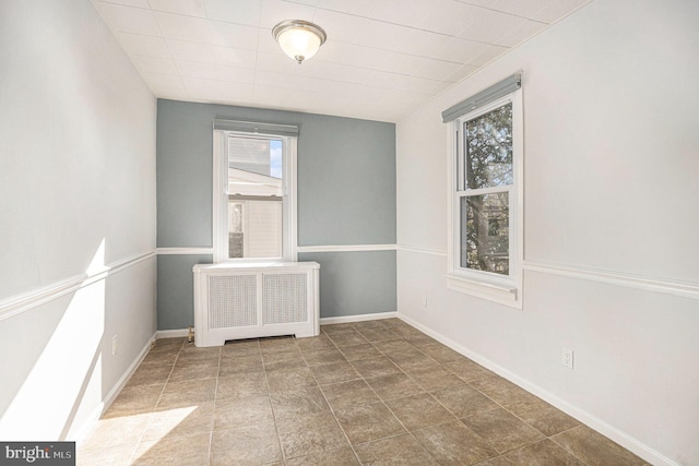 unfurnished room featuring baseboards, plenty of natural light, and radiator heating unit