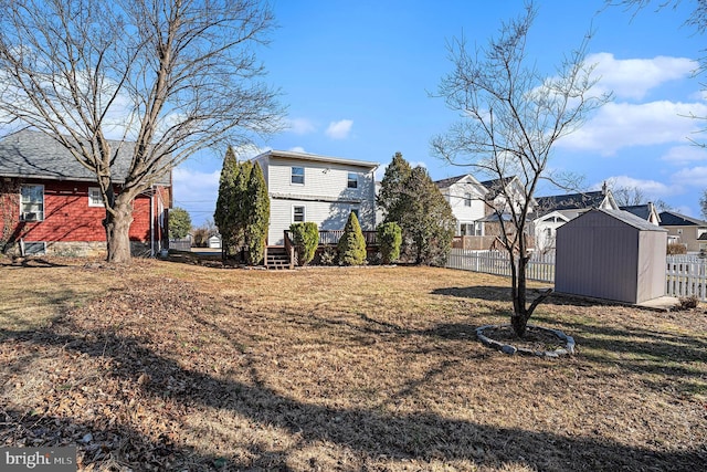 view of yard featuring a storage shed, fence, a residential view, an outdoor structure, and a wooden deck