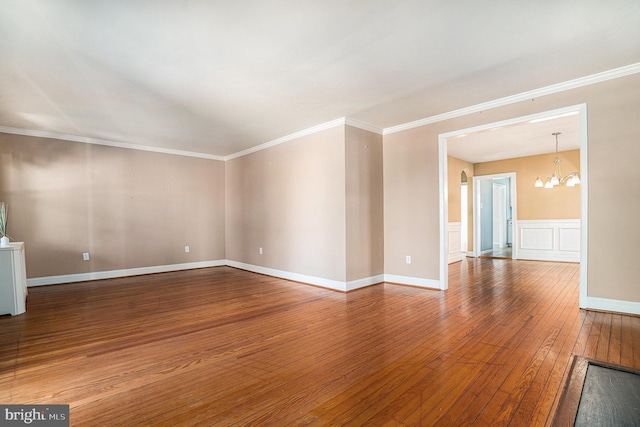 spare room featuring a chandelier, hardwood / wood-style floors, ornamental molding, and a decorative wall