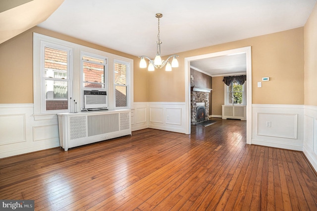 unfurnished dining area featuring hardwood / wood-style floors, radiator heating unit, cooling unit, and a notable chandelier