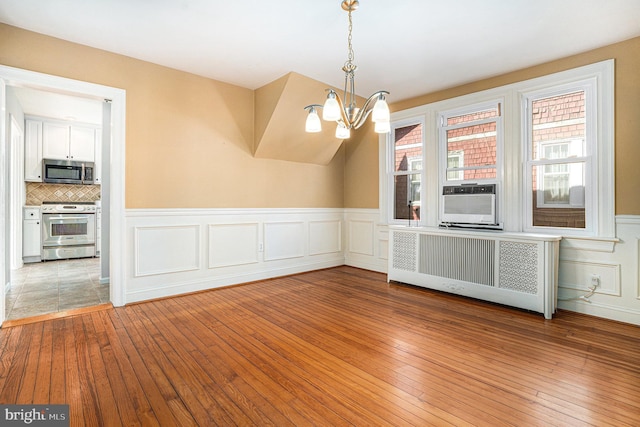 unfurnished dining area with light wood-type flooring, radiator, wainscoting, and an inviting chandelier