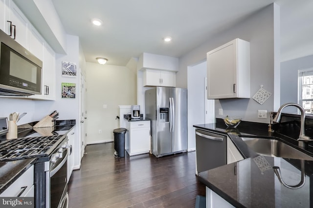 kitchen featuring dark wood finished floors, dark stone countertops, white cabinets, stainless steel appliances, and a sink