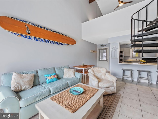 living room with a ceiling fan, light tile patterned flooring, baseboards, a towering ceiling, and stairs