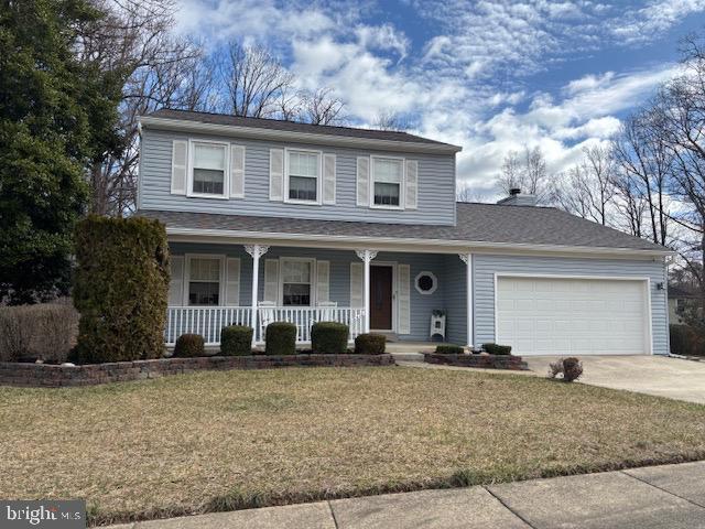 traditional-style house with a front yard, covered porch, driveway, and an attached garage