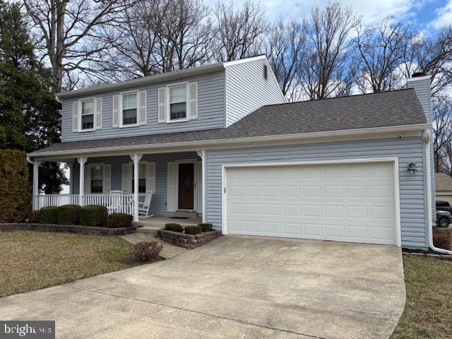 view of front of home with roof with shingles, a chimney, covered porch, concrete driveway, and a garage