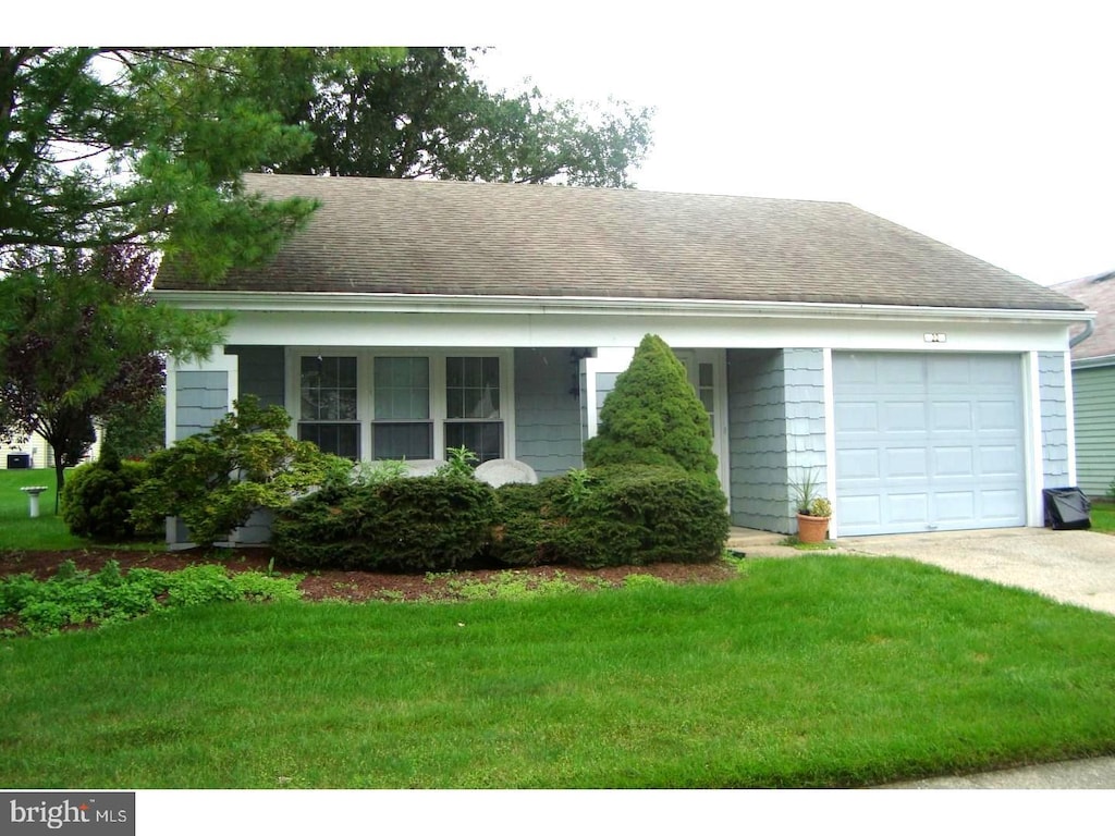 ranch-style home featuring an attached garage, concrete driveway, a front lawn, and a shingled roof