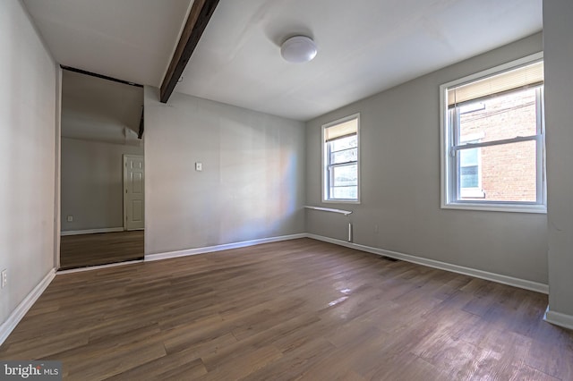 spare room featuring beamed ceiling, baseboards, and wood finished floors