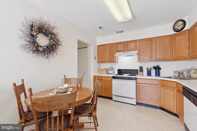 kitchen with visible vents, under cabinet range hood, light floors, white appliances, and a sink