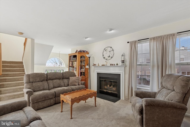 living room with a fireplace with flush hearth, carpet, and stairs