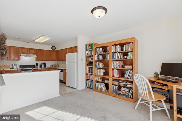 interior space featuring under cabinet range hood, gas range oven, light carpet, freestanding refrigerator, and brown cabinetry