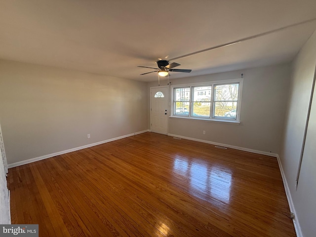 empty room featuring a ceiling fan, visible vents, baseboards, and wood finished floors