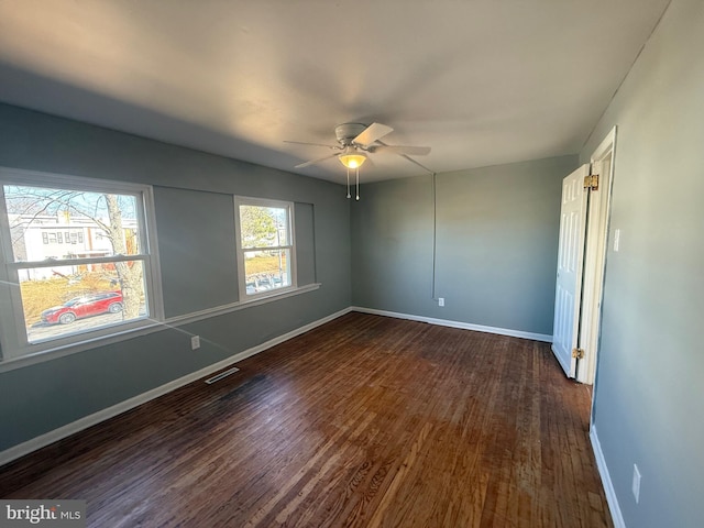 empty room with dark wood-style floors, visible vents, ceiling fan, and baseboards