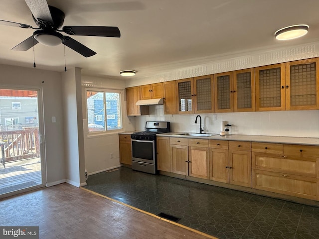 kitchen with under cabinet range hood, a sink, baseboards, light countertops, and stainless steel range with gas cooktop