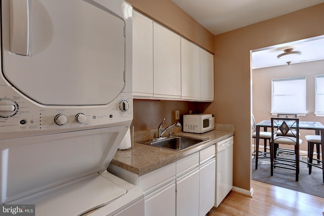 laundry room with stacked washer and clothes dryer, light wood-style flooring, a sink, baseboards, and laundry area