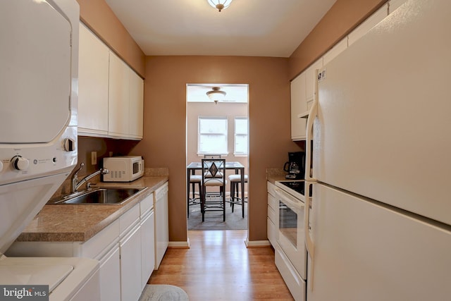 kitchen with stacked washer / dryer, light wood-style flooring, white appliances, white cabinetry, and a sink