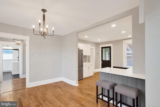 kitchen with white cabinetry, freestanding refrigerator, light wood-style floors, a breakfast bar area, and light countertops