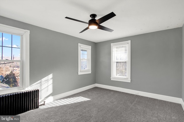 unfurnished room with ceiling fan, radiator heating unit, baseboards, and dark colored carpet