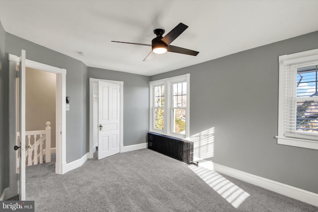 carpeted bedroom with multiple windows, a ceiling fan, radiator heating unit, and baseboards