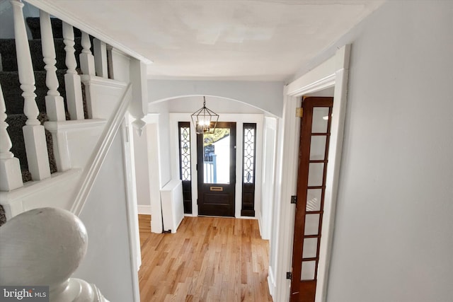 entryway with stairway, a notable chandelier, arched walkways, and light wood-type flooring