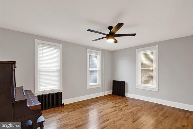 unfurnished room with a ceiling fan, radiator heating unit, wood finished floors, and baseboards