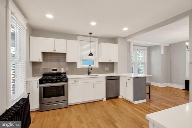 kitchen with a peninsula, radiator heating unit, light countertops, white cabinets, and appliances with stainless steel finishes