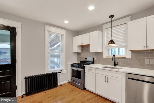 kitchen with a sink, radiator heating unit, stainless steel appliances, white cabinets, and light countertops