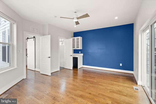 unfurnished bedroom featuring a barn door, baseboards, light wood-style floors, and visible vents