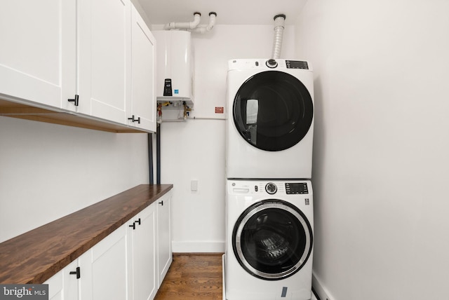 laundry area featuring baseboards, dark wood finished floors, stacked washer and dryer, tankless water heater, and cabinet space